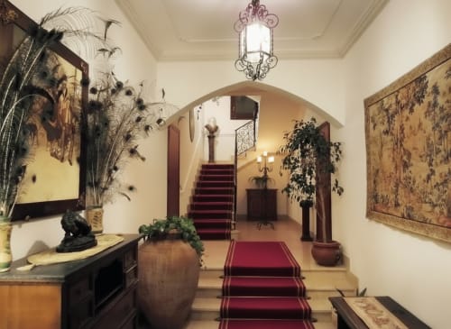 Elegante corridoio dell'Hotel Candalú con moquette rossa, portale ad arco, arazzi decorativi e grande scalone