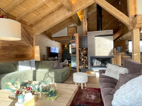 Intérieur chaleureux du chalet en bois des Chalets d'Aline à La Plagne avec cheminée, canapé vert et poutres rustiques