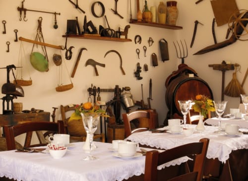 Elegante sala da pranzo dell'Hotel Villa Giardinata Candalú con esposizione di attrezzi agricoli vintage, tavoli drappeggiati di bianco e giardino