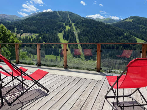 Chaises rouges sur la terrasse des Chalets d'Aline avec vue sur la vallée alpine de La Plagne Tarentaise