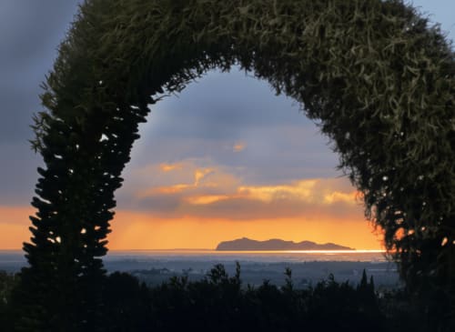 Tramonto visto dall'arco rivestito d'edera del giardino dell'Hotel Candalú di Valderice, con vista sul Mar Mediterraneo e un'isola