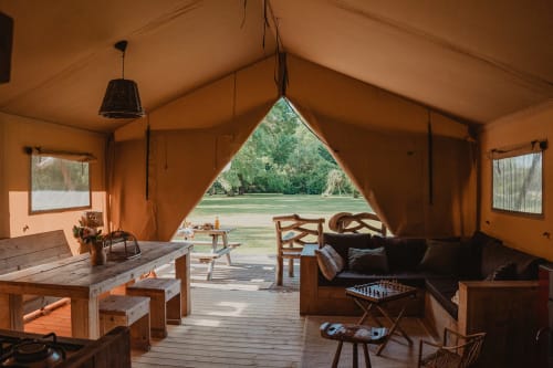 Intérieur de tente safari aux Gîtes de Cormenin avec salon, table à manger et vue sur le jardin par l'entrée en toile ouverte