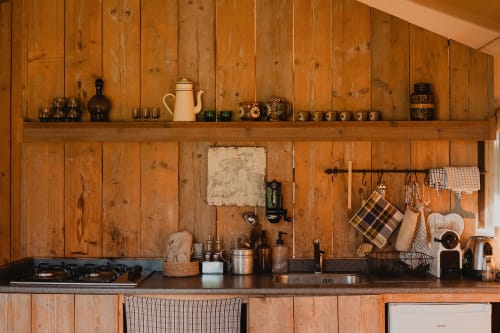 Cuisine rustique en bois avec plan de travail en pierre, étagères, poêle et ustensiles suspendus aux Gîtes de Cormenin