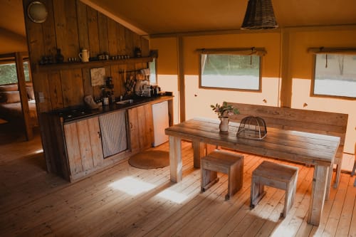 Salle à manger de la tente safari aux Gîtes de Cormenin avec table en bois, bancs et cuisine donnant sur le jardin