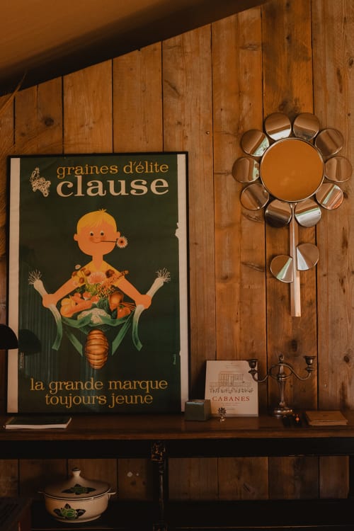 Affiche vintage française « Graines d'élite Clause » exposée au-dessus d'une étagère en bois avec miroir floral en cuivre et objets de décoration