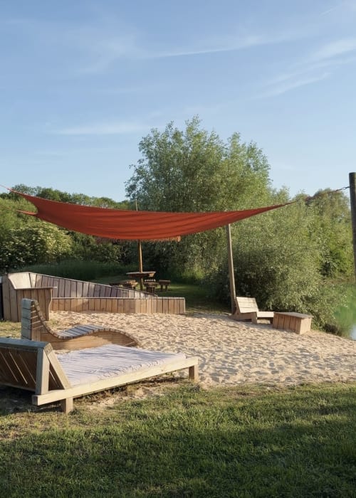 Site de glamping en tente safari aux gîtes de Cormenin avec auvent rouge, zone de sable, transats en bois et vues sur le jardin