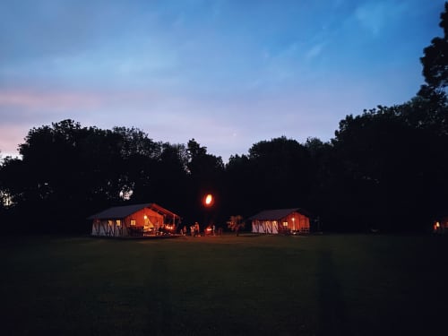 Deux tentes safari illuminées aux gîtes de Cormenin au crépuscule, entourées d'arbres dans le jardin de Saint-Hilaire-sur-Puiseaux