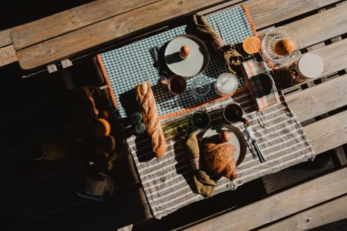 Petit-déjeuner en terrasse aux gîtes de Cormenin : pain, viennoiseries et boissons sur nappe à carreaux, vue sur le jardin
