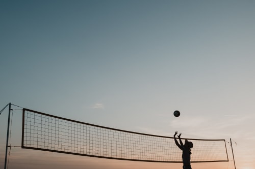 Silhouette d'une personne jouant au volley-ball au coucher du soleil, filet visible contre un ciel dégagé aux Gîtes de Cormenin