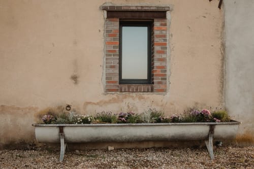 Villa rustique aux Gîtes de Cormenin : fenêtre en brique patinée, jardinière en pierre avec fleurs colorées et allée gravillonnée