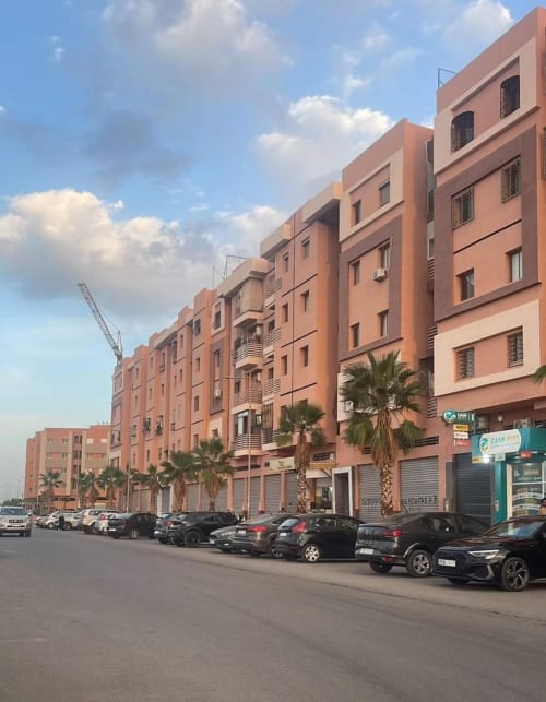 Façade de l'hôtel Eucalyptus Ethnic à Essaouira avec ses bâtiments en terre cuite, voitures garées et palmiers sous ciel bleu