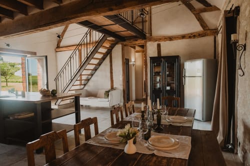 Salle à manger de villa moderne avec poutres en bois, table dressée, cuisine ouverte et escalier aux Gîtes de Cormenin près du lac