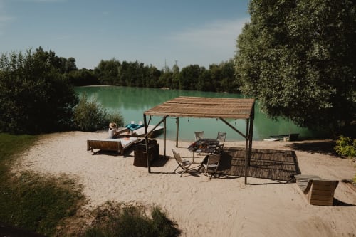 Zone de plage sablonneuse aux gîtes de Cormenin avec cabane en bois, sièges et vue sur le lac turquoise entouré d'arbres