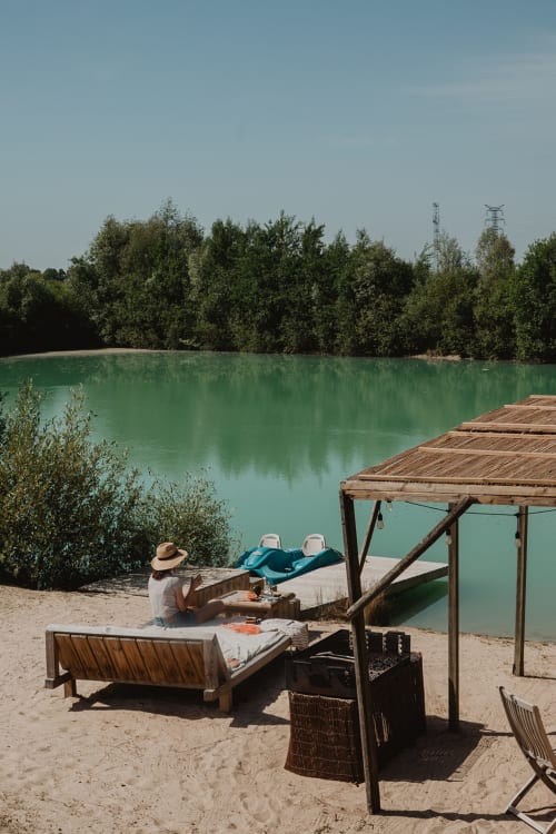 Femme relaxante sur transat à la villa Les gîtes de Cormenin avec vue sur lac turquoise, terrasse en bois et arbres