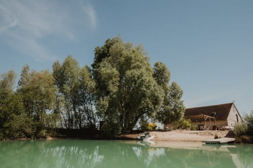 Villa au bord du lac aux Gîtes de Cormenin avec vue sur l'eau verte, arbres et maison rustique à Saint-Hilaire-sur-Puiseaux