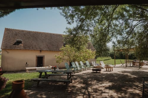 Patio extérieur de la villa Les gîtes de Cormenin avec chaises longues, tables de pique-nique, foyer et arbres d'ombrage