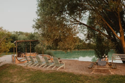 Coin détente au bord du lac de la villa Les gîtes de Cormenin avec chaises Adirondack, pergola et foyer donnant sur l'eau calme