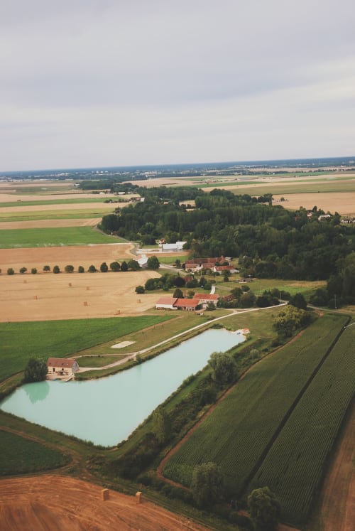 Vue aérienne du gîte Les gîtes de Cormenin à Saint-Hilaire-sur-Puiseaux, entouré de terres agricoles et d'une eau turquoise