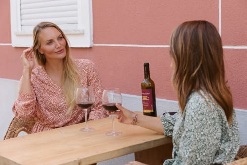 Duas mulheres apreciando vinho na Coastline Rentals Portugal, uma propriedade costeira com paredes rosa e área de estar ao ar livre