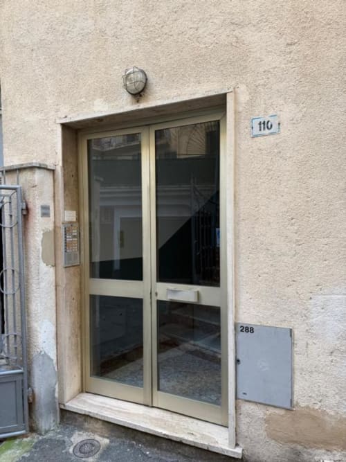 Ingresso con porta in vetro color crema dell'appartamento TuffonelBlu a Sanremo, numero 110, con facciata in pietra e applique murale