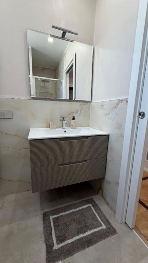 Elegante vanity da bagno con lavabo bianco, mobile scuro in stile trama, rivestimento in marmo e specchio presso TuffonelBlu, Sanremo