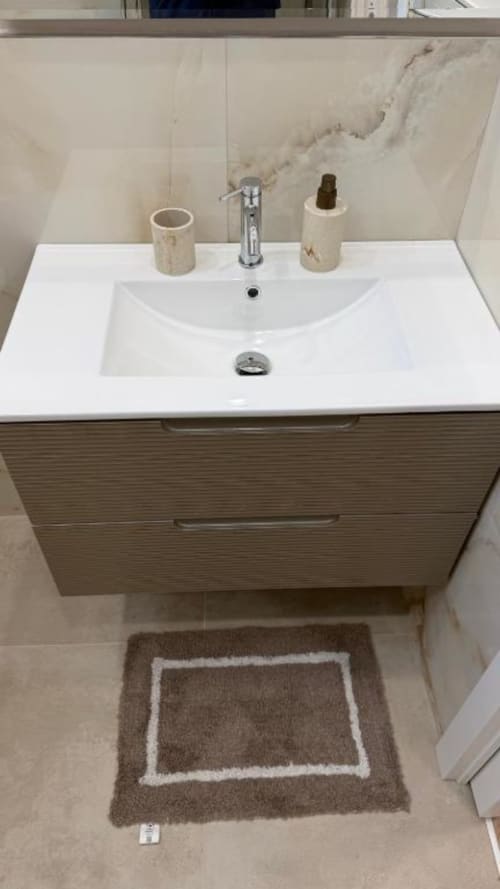 Moderno lavabo da bagno con bacile bianco, rubinetto cromato, accessori beige e rivestimento in marmo nell'appartamento TuffonelBlu