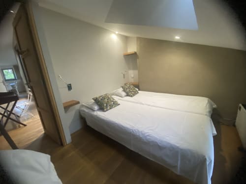 Chambre Le Perchoir du AJOUCADOU B&B à Lourmarin : lit blanc, coussins décoratifs, parquet et plafond mansardé