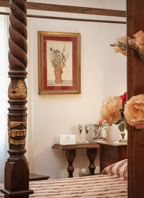 Elegante suite dell'Hotel Candalú con colonna in legno intagliato, arte botanica incorniciata, rose color pesca, flute di champagne
