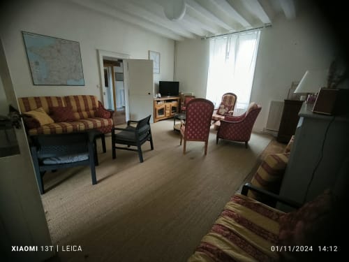 Séjour du Gîte de la Vallée avec sièges rayés, fauteuils, télévision et grandes fenêtres lumineuses à Courdemanche