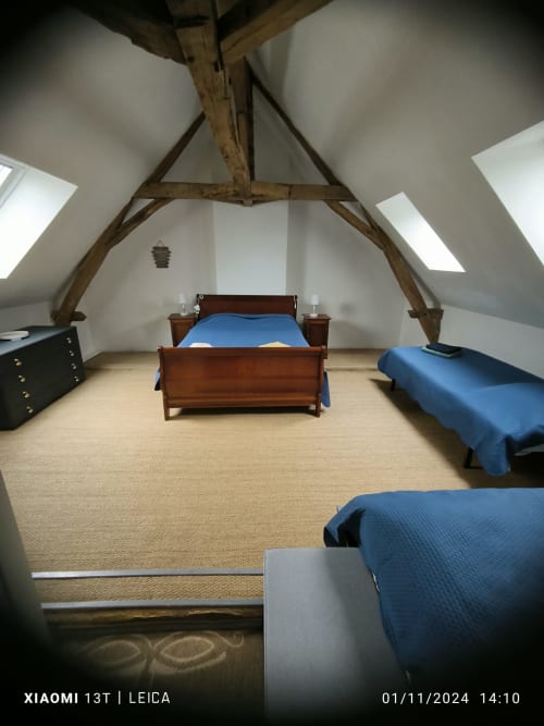 Chambre mansardée du Gîte de la vallée avec poutres apparentes, trois lits, fenêtres de toit et mobilier en bois