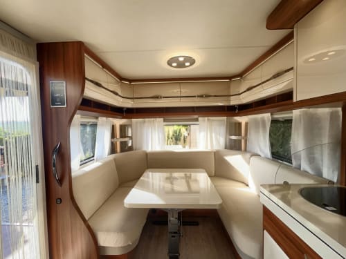 Interior de autocaravana de lujo en B&B Wine And Cooking Penedès con asientos crema, mesa de comedor y detalles de madera