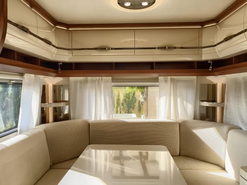 Interior moderno y luminoso de autocaravana con asientos en tonos crema, detalles en madera y amplios ventanales en B&B Wine And Cooking Penedès, Barcelona