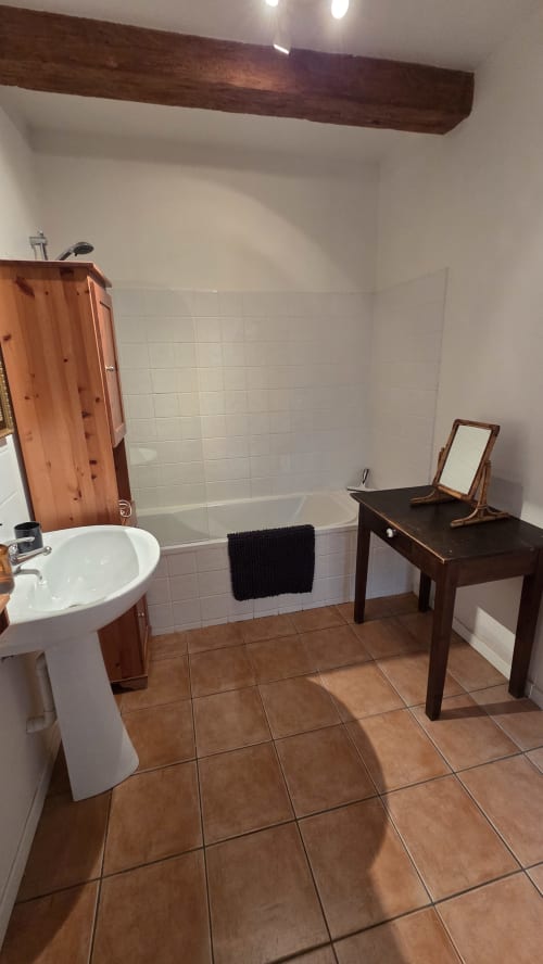Spacious bathroom in Le Surcouf apartment at Manoir de la Bégaudière with bathtub, pedestal sink, and wooden furnishings