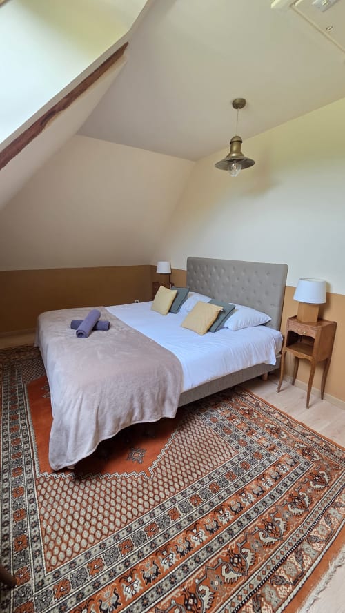 Spacious attic bedroom at Manoir de la Bégaudière with queen bed, grey headboard, wooden beams, pendant light, and oriental