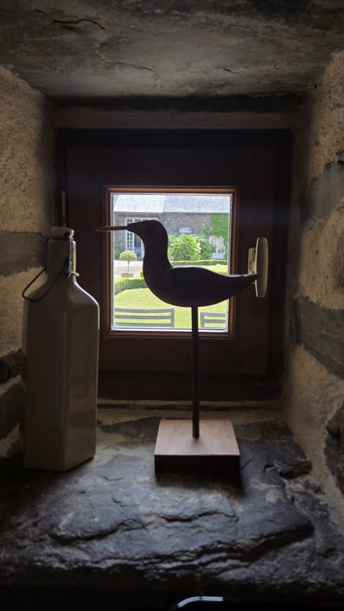 Modern bird sculpture silhouette framing garden view through stone corridor at Manoir de la Bégaudière, Mont-Dol
