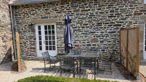 Stone patio with dining table and chairs, closed umbrella, flowers, at Manoir de la Bégaudière in Mont-Dol