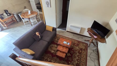 Cozy living room at Manoir de la Bégaudière with dark sofa, wooden TV stand, ornate rug, and dining area visible in