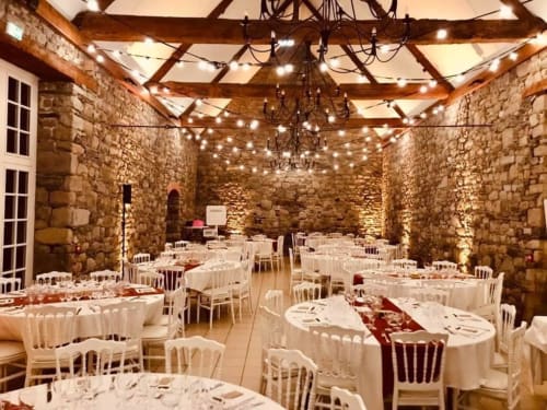 Elegant banquet hall at Manoir de la Bégaudière with stone walls, exposed beams, and string lights in Mont-Dol