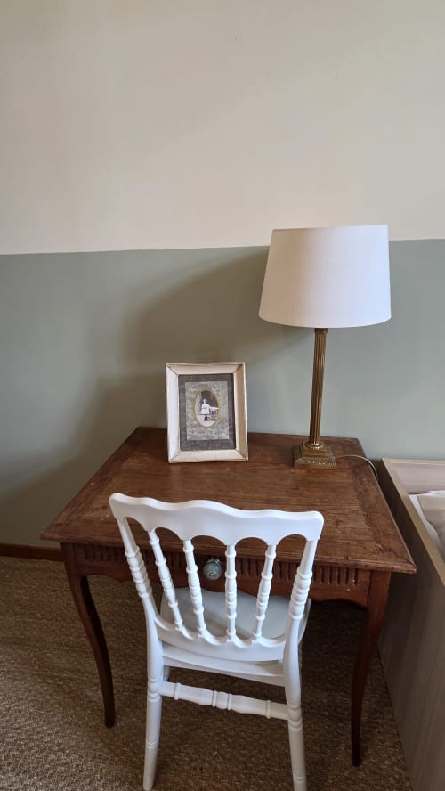 Workspace at Manoir de la Bégaudière with wooden desk, white chair, framed photo, brass lamp, and garden view in Mont-Dol