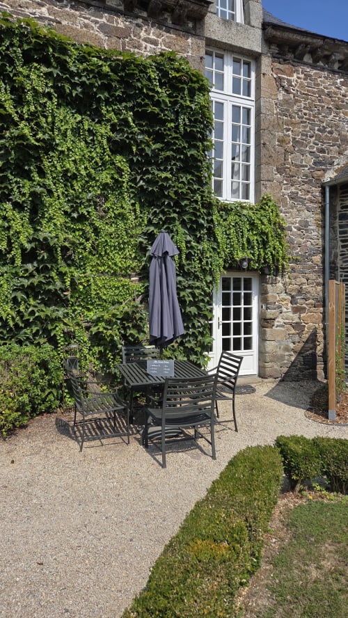 Ivy-covered stone courtyard at Manoir de la Bégaudière with dining table, chairs, and umbrella in Mont-Dol