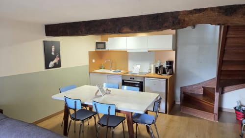 Modern apartment kitchen and dining area with white table, blue chairs, wooden beams at Manoir de la Bégaudière, Mont-Dol