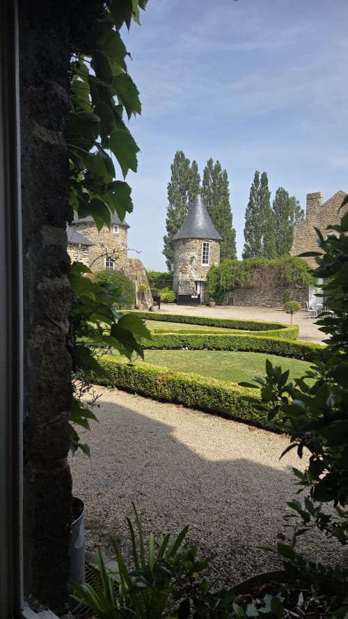 Manoir de la Bégaudière garden view with stone buildings, tower, manicured hedges and poplar trees in Mont-Dol
