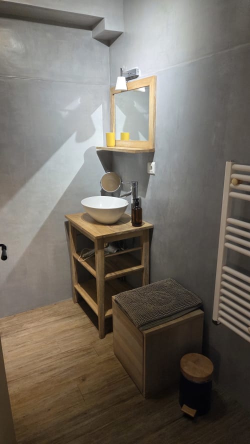 Modern bathroom with vessel sink on wooden vanity, mirror with shelf, concrete walls, and heated towel rack at Manoir de la