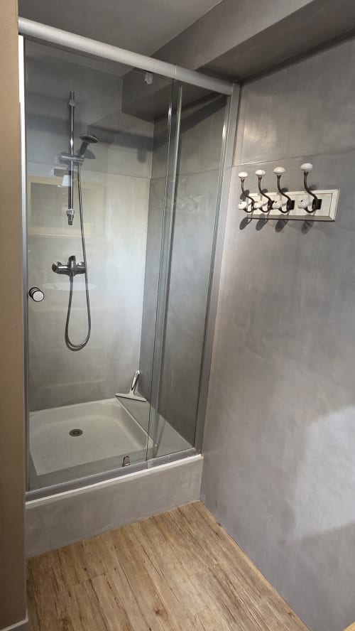 Modern shower enclosure with glass doors, rainfall showerhead, and four wall hooks in Le Duguay Trouin apartment at Manoir de
