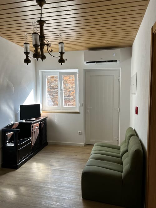 Sala de estar moderna em Casas do Sinhel com sofá verde, TV, lustre e vistas de montanha pela janela
