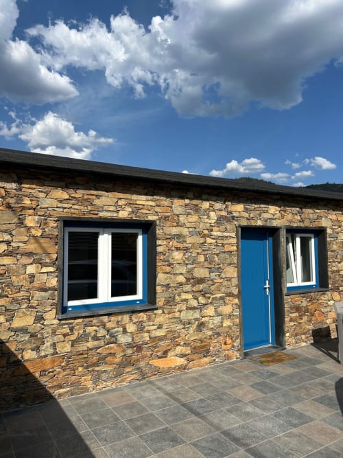 Casa das Rodas em Alvares: chalé com porta azul, paredes de pedra e vistas das montanhas sob céu limpo