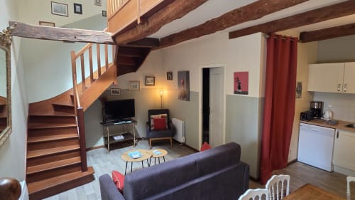 Cozy apartment living room at Manoir de la Bégaudière with wooden staircase, sofa, TV, and open kitchen in Mont-Dol