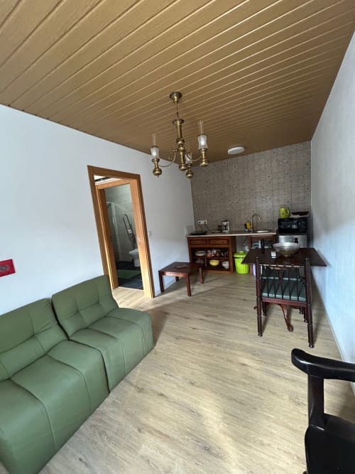 Sala de estar da Casa das Rodas com sofá verde, kitchenette, mesa de jantar e teto de madeira em Casas do Sinhel, Alvares