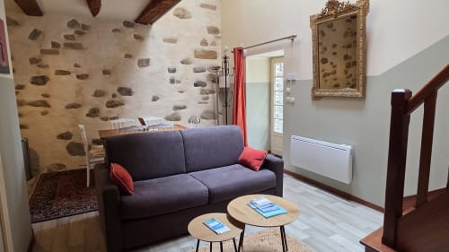 Modern apartment living room at Manoir de la Bégaudière with purple sofa, wooden tables, stone accent wall, and garden view