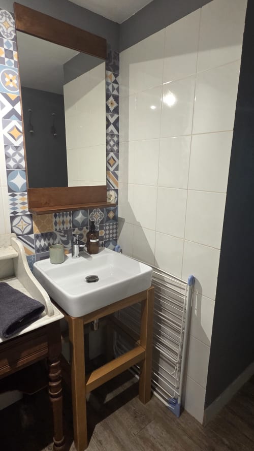 Modern bathroom at Manoir de la Bégaudière with white tiles, wooden vanity, patterned accent wall, and mirror